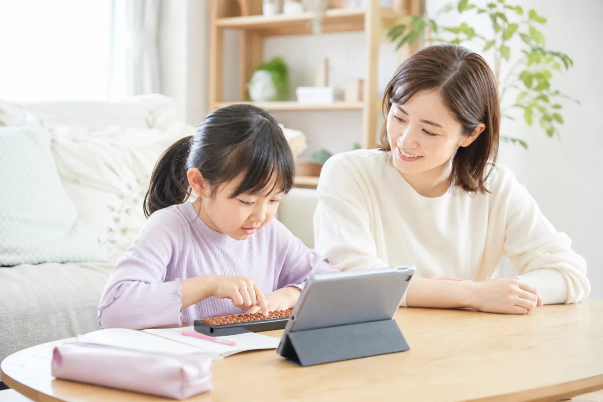 自宅でタブレットを見ながらそろばんを練習する女の子とママ