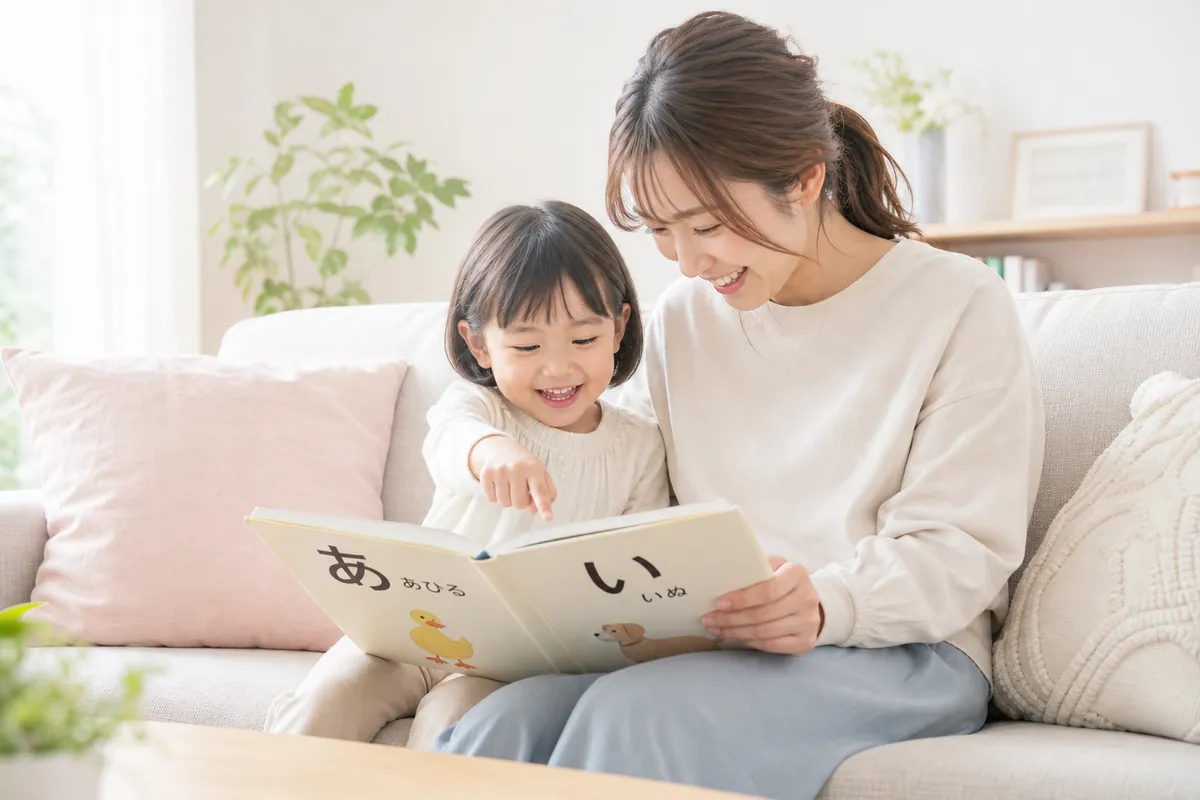 ママと一緒に絵本のひらがなを指さす子ども