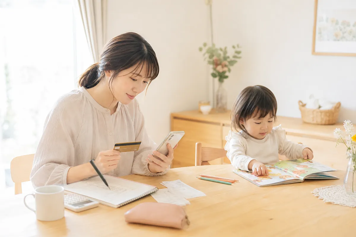 カードと家計アプリを見ながら家計を管理するママ
