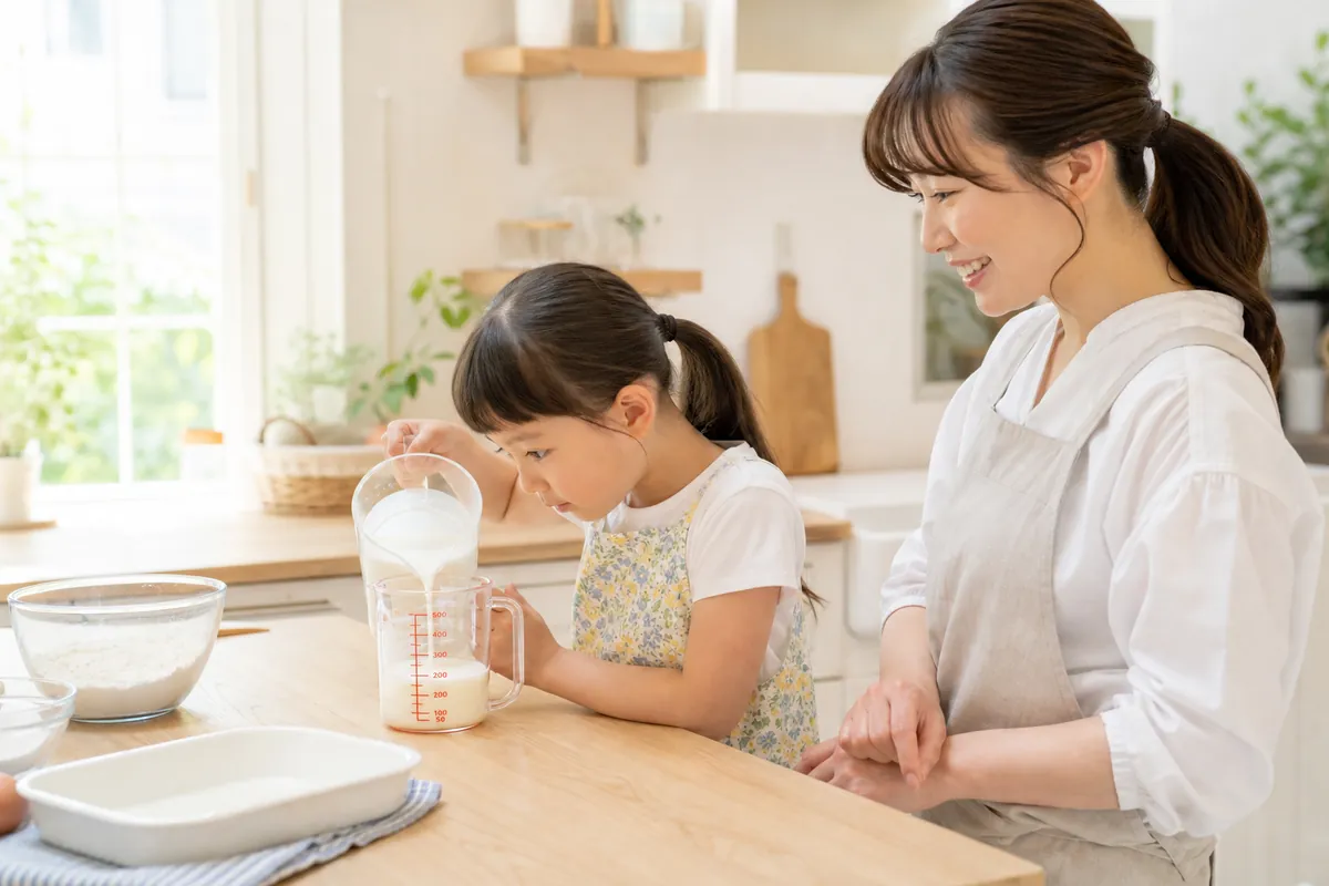 計量カップの目盛りを見ながら料理を手伝う小学生