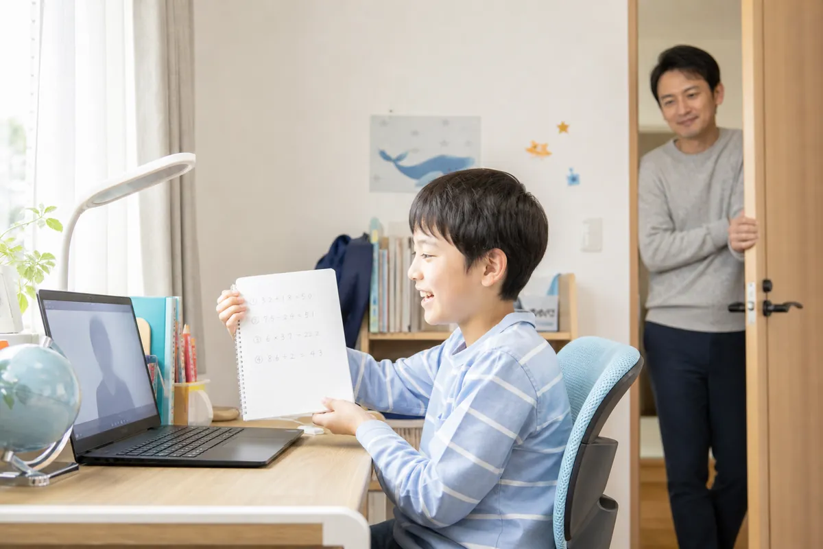 ノートを見せながらオンライン家庭教師の授業を受ける小学生の男の子とパパ